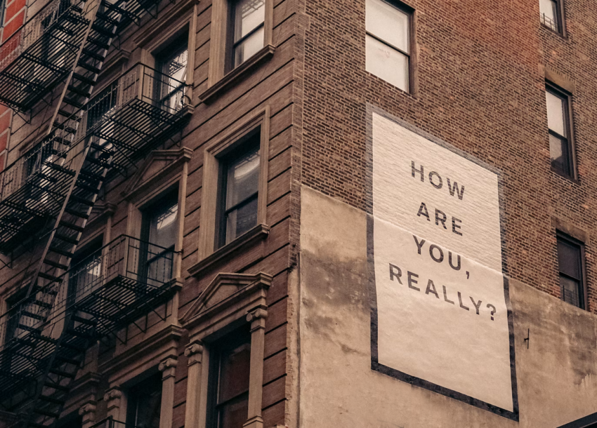 Photograph : old concrete building during daytime, with large typography poster with text ‚HOW ARE YOU REALLY'