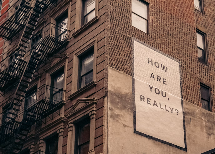 Photograph : old concrete building during daytime, with large typography poster with text ‚HOW ARE YOU REALLY'